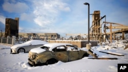 Snow left by a fast-moving winter storm covers the charred remains of a vehicle destroyed by wildfires in the parking lot of the Element hotel, which was also burned, Jan. 6, 2022, in Superior, Colo. 