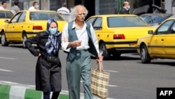 FILE - An elderly man and a woman, wearing a protective mask, walk along a street in Iran's capital Tehran on March 15, 2020. 