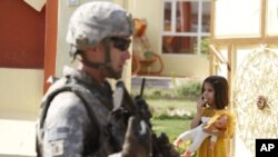 A U.S. soldier attached to the Golden Lions forces walks past a girl carrying her doll, during a patrol in the city of Kirkuk, July 20, 2011