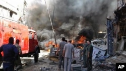 Quelques personnes se rassemblent autour des bâtiments en feu après une attaque à la bombe dans la banlieue de Sayyida Zeinab, à Damas, Syrie, 11 juin, 2016.