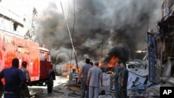 Quelques personnes se rassemblent autour des bâtiments en feu après une attaque à la bombe dans la banlieue de Sayyida Zeinab, à Damas, Syrie, 11 juin, 2016. (SANA via AP)