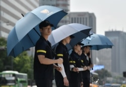 FILE - Police officers use umbrellas to protect themselves from the sun while anti-war activists hold a rally against planned South Korea-U.S. annual joint military exercises near the U.S. embassy in Seoul, Aug. 5, 2019.