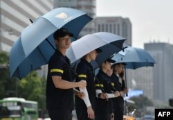 FILE - Police officers use umbrellas to protect themselves from the sun while anti-war activists hold a rally against planned South Korea-U.S. annual joint military exercises near the U.S. embassy in Seoul, Aug. 5, 2019.