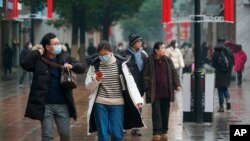 Masked pedestrians walk down a shopping street in downtown Wuhan, China, Wednesday, Jan. 22, 2020. The number of cases of a new coronavirus from Wuhan has risen over 400 in China and the death toll to 9, Chinese health authorities said.