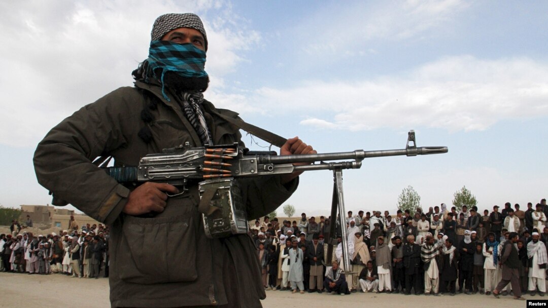 FILE - Seorang anggota Taliban dan orang lain berdiri di lokasi saat eksekusi tiga pria di Provinsi Ghazni, Afghanistan, 18 April 2015. Pada 22 Februari 2024, otoritas Taliban secara terbuka mengeksekusi dua pria yang dihukum karena pembunuhan dalam kasus terpisah.