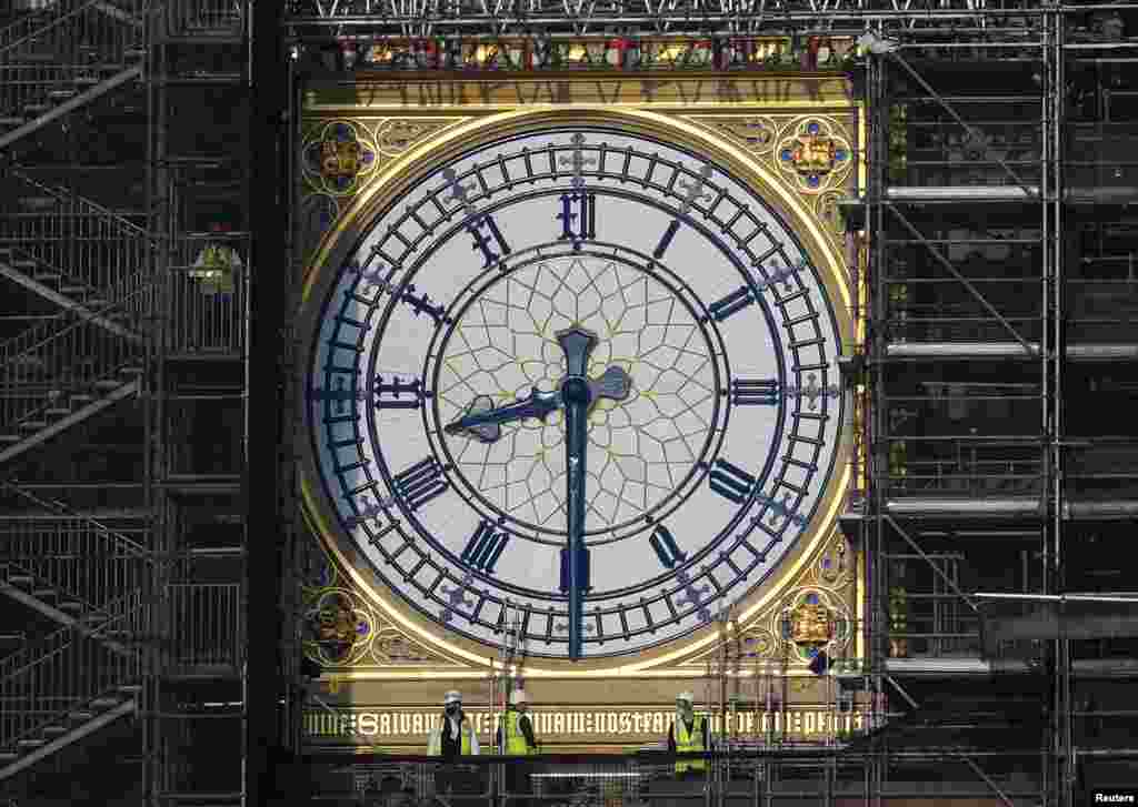 Workers stand on scaffolding underneath one of the clock faces on the Elizabeth Tower or Big Ben as hands and dials are seen restored to the original Prussian blue coloring, while renovation works continue at the Houses of Parliament in London.