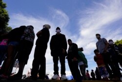 FILE - Migrants line up for a free meal at a makeshift camp of migrants at the border port of entry leading to the United States, March 17, 2021, in Tijuana, Mexico.