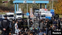 FILE- Bosnian and Croatian border police stand guard in front of migrants at Maljevac border crossing between Bosnia and Croatia near Velika Kladusa, Bosnia, Oct. 24, 2018. 