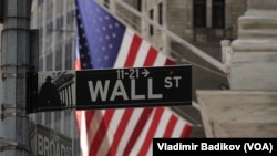 Tanda Wall Street di New York, dengan latar belakang bendera AS, terlihat di persimpangan Broad St dan Wall St pada September 2024. (Foto: VOA)