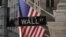 Tanda Wall Street di New York, dengan latar belakang bendera AS, terlihat di persimpangan Broad St dan Wall St pada September 2024. (Foto: VOA)