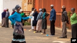 A worker wearing a face mask and gloves to protect herself against coronavirus, joins the queue to receive her social grant outside a pay point in Thokoza, east of Johannesburg, South Africa, March 30, 2020. 