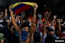 FILE - Protesters react in front of a fire burning at the entrance of a building, housing the magistracy of the Supreme Court of Justice and a bank branch, during a rally against Venezuela's President Nicolas Maduro, in Caracas, Venezuela, June 12, 2017.