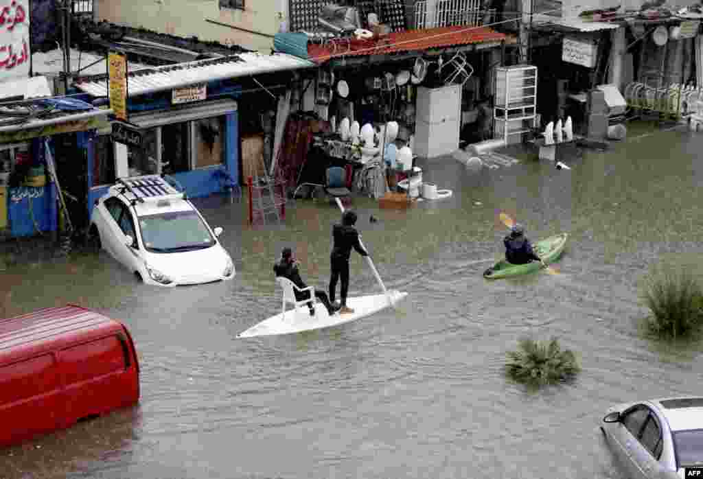 Lebanese men use a paddle board and canoe as means of transportation on a flooded road due to heavy rain, at the southern entrance of the capital Beirut.