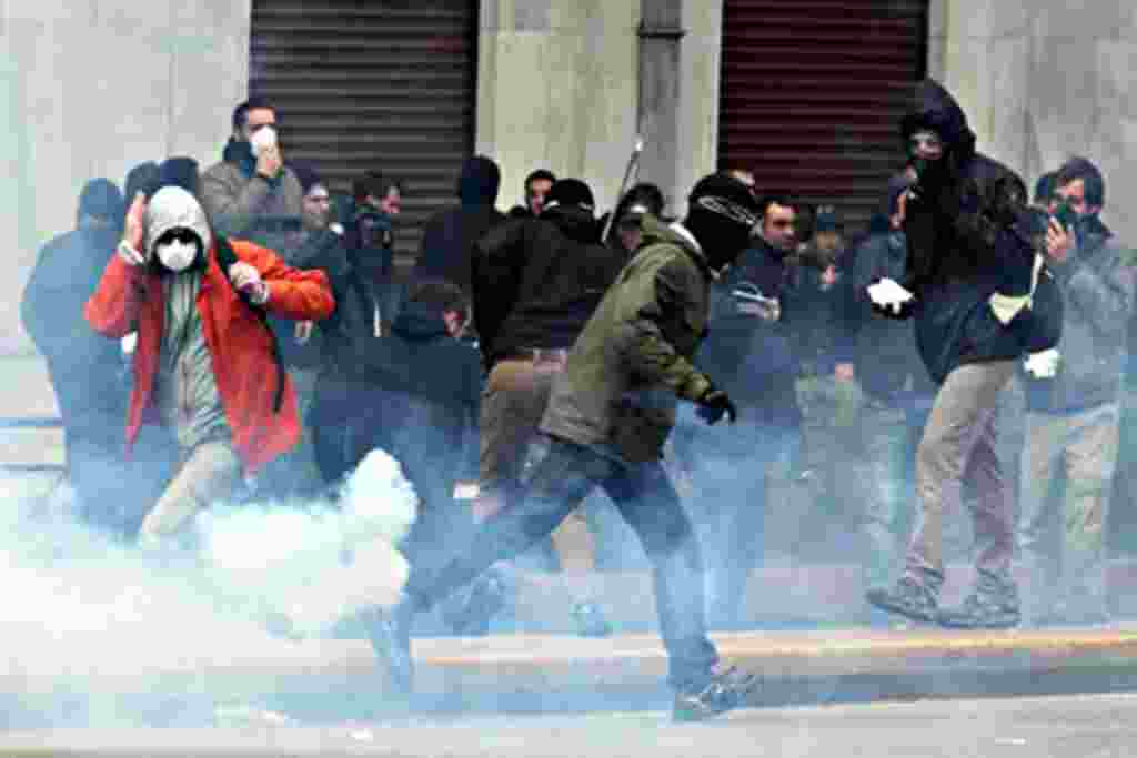 Protesters try to avoid a tear gas canister during clashes in central Athens, February 23, 2011