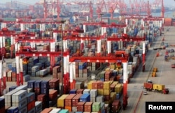 FILE - Trucks drive past piles of shipping containers at the Qingdao port in Qingdao, Shandong province, June 8, 2014.