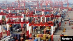 FILE - Trucks drive past piles of shipping containers at the Qingdao port in Qingdao, Shandong province, June 8, 2014.