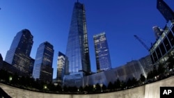 In this image made with a fisheye lens, One World Trade Center, center, rises above waterfalls at the National September 11 Memorial and Museum, Sept. 8, 2013, in New York.