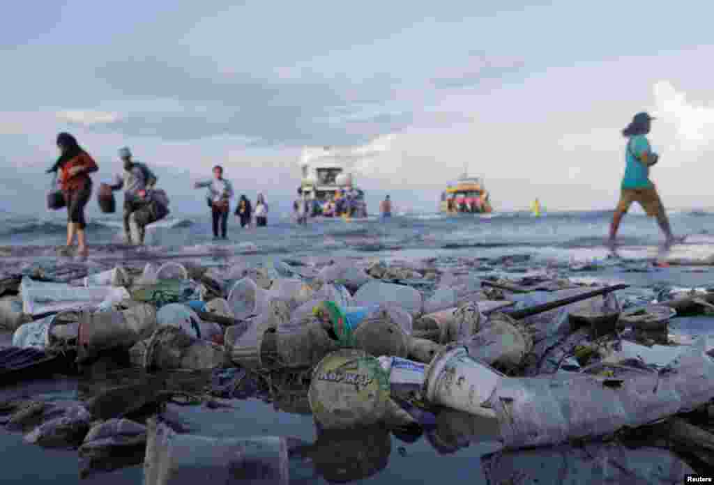 Tourists and local residents disembark a boat coming from nearby Nusa Penida island as plastic trash pollutes the beach in Sanur, Denpasar, Bali, Indonesia.