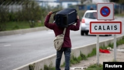 FILE - A migrant carries his belongings as he departs a camp in Calais, France, Oct. 22, 2016.