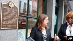 Erin Greenwald, who led a project to develop markers for sites involved in the New Orleans slave trade and a smartphone app to tour such sites, demonstrates the app on Sept. 27, 2018 in New Orleans. She and Laura Tennyson, producer for the app, are standing near a marker.