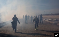 Migrants run from tear gas launched by U.S. agents, amid photojournalists covering the Mexico-U.S. border, after a group of migrants got past Mexican police at the Chaparral crossing in Tijuana, Nov. 25, 2018.