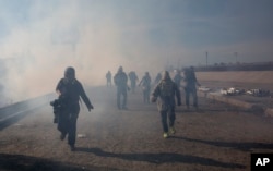 Migrants run from tear gas launched by U.S. agents, amid photojournalists covering the Mexico-U.S. border, after a group of migrants got past Mexican police at the Chaparral crossing in Tijuana, Mexico, Nov. 25, 2018.