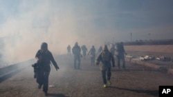 Migrants run from tear gas launched by U.S. agents, amid photojournalists covering the Mexico-U.S. border, after a group of migrants got past Mexican police at the Chaparral crossing in Tijuana, Mexico, Sunday, Nov. 25, 2018.