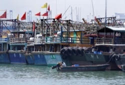 FILE - A fisherman lifts the propeller up next to anchored boats at a fishing harbor in Shenzhen, China, Sept. 15, 2018.