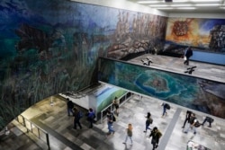 People walk under murals representing the foundation of the Aztec capital city of Tenochtitlan, in the Tacubaya metro station in Mexico City, Tuesday, May 18, 2021. The capital of the Aztec empire, now known as Mexico City, fell to Spanish Conquistador He