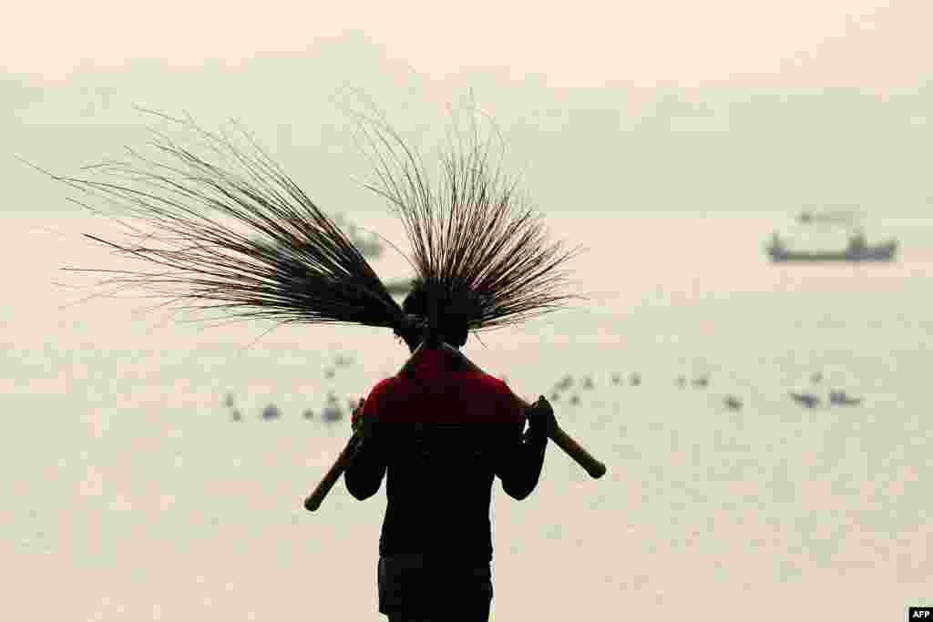 An Indian laborer carries a pair of brooms while cleaning at the Sangam, the confluence of the three rivers Ganges, Yamuna and mythical Saraswati, ahead of the annual Magh Mela festival in Allahabad.