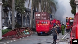 Firefighters stand across from the main entrance of Tan Than Industries as the Taiwanese bicycle factory burns in Binh Duong