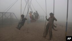 Anak-anak bermain ayunan di taman yang diselimuti kabut asap di Lahore, Pakistan, 11 November 2017.