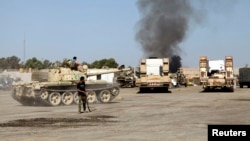 Smoke is seen rising from the Brigade Qaqaa headquarters, a former Libyan Army camp known as Camp 7 April, behind members of the Libya Shield, following clashes between rival militias at the Sawani road district in Tripoli, Aug. 24, 2014. 