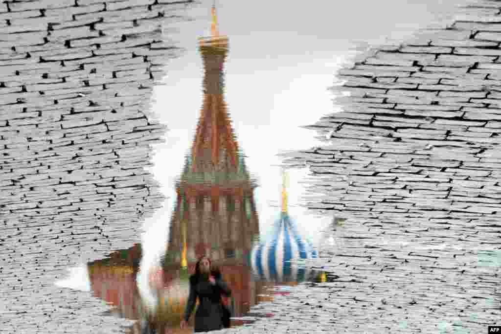This photo, rotated 180 degrees, shows a woman reflected in a puddle as she walks past landmark St.Basil&#39;s Cathedral at the Red Square in Moscow, Russia.