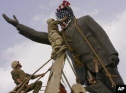 FILE - An Iraqi man, bottom right, watches Cpl. Edward Chin of the 3rd Battalion, 4th Marines Regiment, cover the face of a statue of Saddam Hussein with an American flag before toppling the statue in downtown in Baghdad, Iraq, April 9, 2003.
