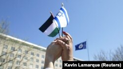  Dua orang bergandengan tangan untuk menyatukan bendera Israel dan Palestina selama demonstrasi di luar Departemen Luar Negeri AS, kantor Menteri Luar Negeri Colin Powell, di Washington, 11 April 2002. (Foto: REUTERS/Kevin Lamarque KL)