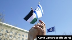  Dua orang bergandengan tangan untuk menyatukan bendera Israel dan Palestina selama demonstrasi di luar Departemen Luar Negeri AS, kantor Menteri Luar Negeri Colin Powell, di Washington, 11 April 2002. (Foto: REUTERS/Kevin Lamarque KL)