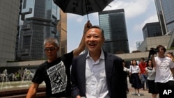 FILE - Occupy Central leader Benny Tai, center, is accompanied by a supporter who raises an umbrella as he leaves high court in Hong Kong, Aug. 15, 2019. 