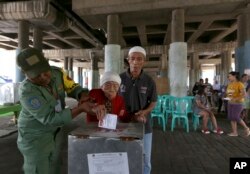 Electoral workers help an elderly woman cast her ballot at a makeshift polling station under a bridge during the runoff election in Jakarta, Indonesia, April 19, 2017.