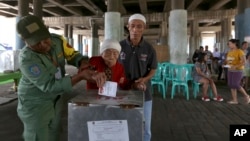 Electoral workers help an elderly woman cast her ballot at a makeshift polling station under a bridge during the runoff election in Jakarta, Indonesia, April 19, 2017. 