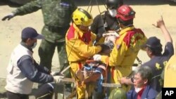 In this image made from video, Lee Tsung-tien, 42, is attended to by rescue workers after he was pulled out conscious from a building which collapsed after an earthquake in Tainan, Taiwan, Monday, Feb. 8, 2016. (AP Photo/APTN) 