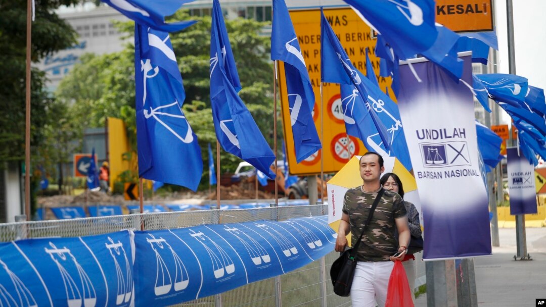 Para pejalan kaki berjalan melintasi bendera koalisi partai berkuasa, Barisan Nasional, di Kuala Lumpur, Malaysia, 10 April 2018. 