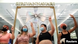 Protest leaders wearing crop tops and showing the three-finger salute, pose in front of Thailand's Princess Sirivannavari fashion boutique at Siam Paragon shopping center, as they protest against the monarchy, in Bangkok, Dec. 20, 2020.