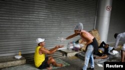 Un miembro de un grupo de residentes del barrio marginal de Chapeu Mangueira, en Brasil, rocía alcohol en la mano de una persona sin hogar mientras le entrega comida en la playa de Copacabana en Río de Janeiro, el 11 de abril de 2020.