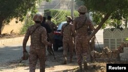 Paramilitary forces and police take cover behind a wall during an attack on the Chinese consulate, where blasts and shots are heard, in Karachi, Pakistan, Nov. 23, 2018. 