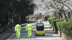 Security personnel walk next to a 5G enabled autonomous vehicle, installed with a camera filming blooming cherry blossoms for an online live-streaming session, inside the closed Wuhan University, in Wuhan, the epicenter of the novel coronavirus outbreak, Hubei province, China March 17, 2020. China Daily via REUTERS