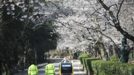 Security personnel walk next to a 5G enabled autonomous vehicle, installed with a camera filming blooming cherry blossoms for an online live-streaming session, inside the closed Wuhan University, in Wuhan, the epicenter of the novel coronavirus outbreak, Hubei province, China March 17, 2020. China Daily via REUTERS