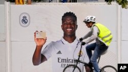 Un ciclista pasa frente a un afiche de Vinicius Junior, el delantero brasileño del Real Madrid, frente al estadio Santiago Bernábeu, el lunes 22 de mayo de 2023 en Madrid.