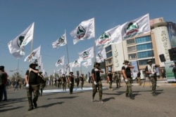 FILE - Iraqi Popular Mobilization Forces march as they hold Popular Mobilization flags in Baghdad, Iraq, May 31, 2019. Iraq's government is placing Iran-backed militias under the full command of the Iraqi armed forces.