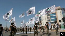FILE - Iraqi Popular Mobilization Forces march as they hold Popular Mobilization flags in Baghdad, Iraq, May 31, 2019. Iraq's government is placing Iran-backed militias under the full command of the Iraqi armed forces.